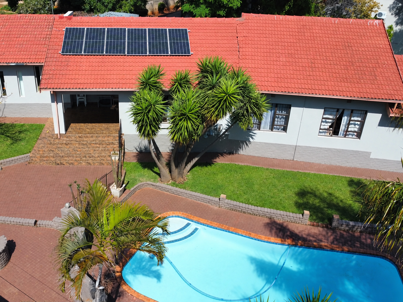 Aerial view of a residential property featuring a tiled roof with solar panels, a swimming pool, and a paved outdoor entertainment area.