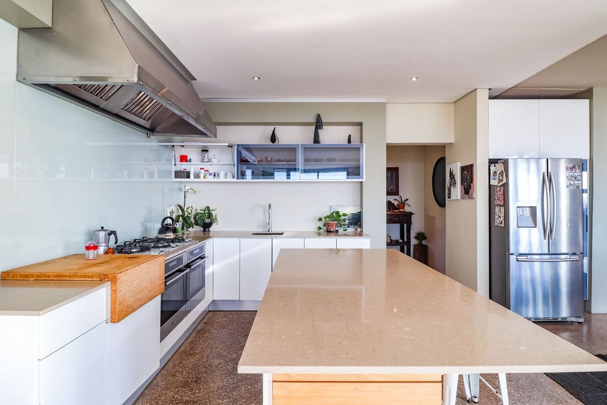 Modern kitchen featuring a large stone island, stainless steel gas cooktop, built-in oven, glass splashback, and ample white cabinetry.