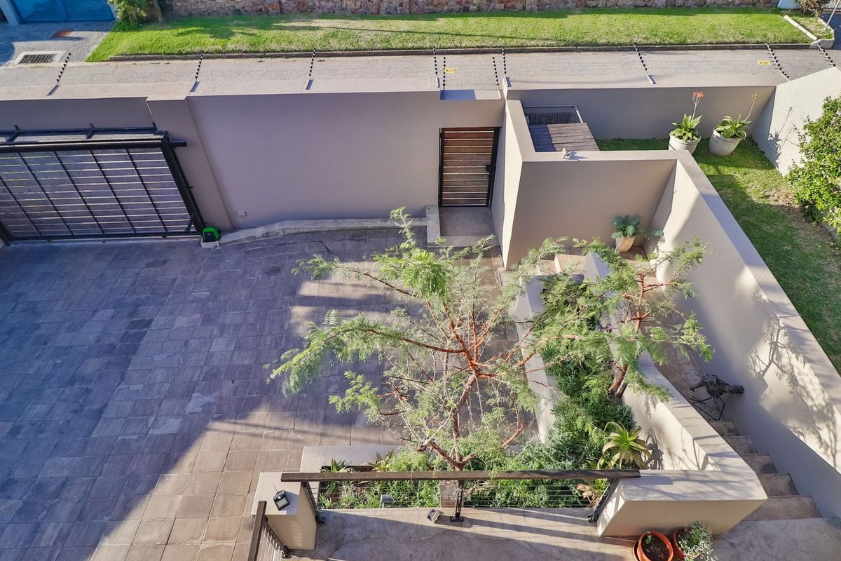 Aerial view of a secure property entrance featuring a paved driveway, electric gate, perimeter wall with electric fencing, and landscaped garden areas.
