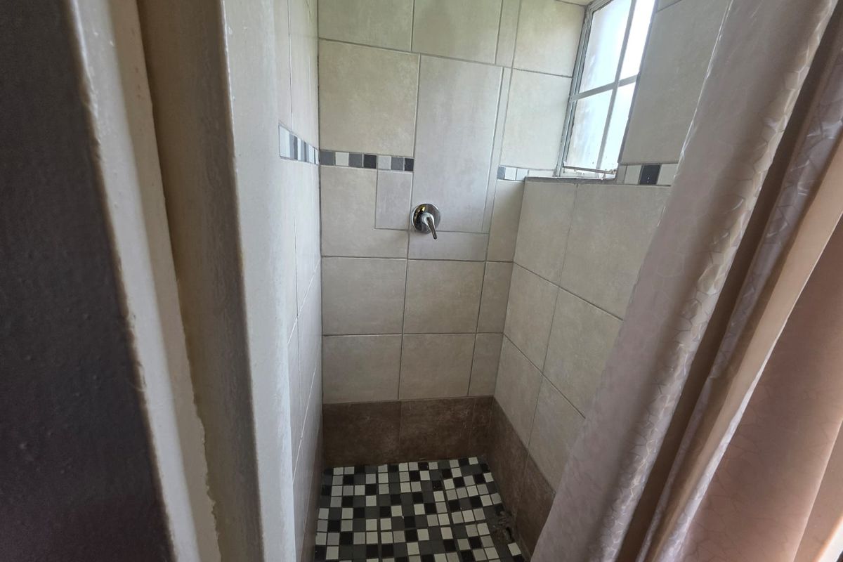 A compact shower enclosure featuring tiled walls, mosaic floor tiling, and a built-in shower mixer.