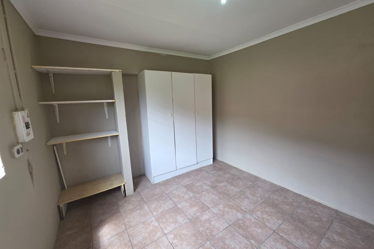 A simple bedroom featuring tiled flooring, a built-in wardrobe, and open shelving, offering a functional space ready for personalization.