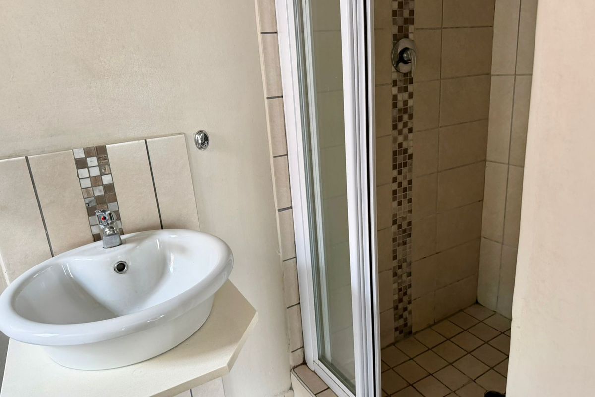 A functional bathroom featuring a pedestal washbasin with tiled splashback and a separate shower enclosure with tiled walls and flooring.