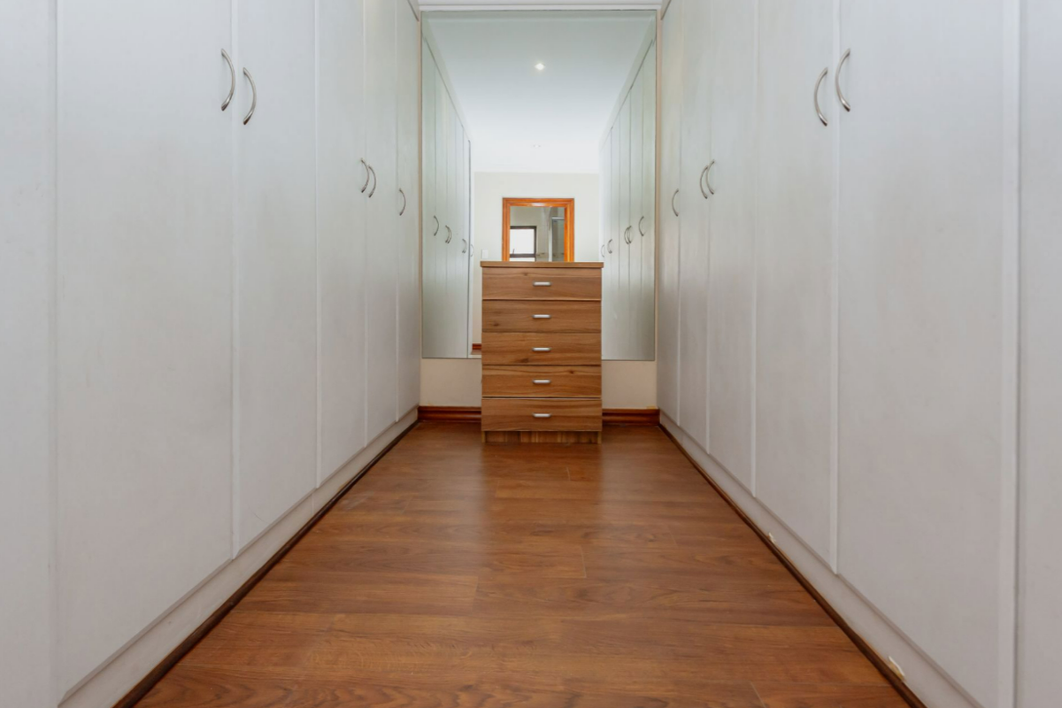 A well-maintained walk-in dressing area featuring extensive floor-to-ceiling built-in cupboards, laminate flooring, and a central full-length mirror.
