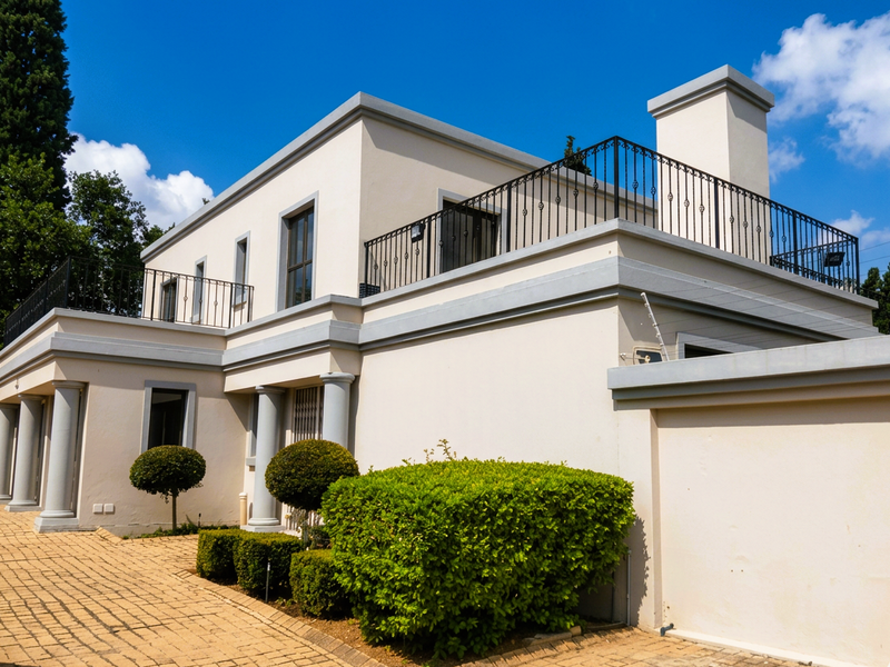 A well-maintained double-story cluster home featuring a paved driveway, classic columns, and a spacious upper-level balcony with wrought iron railings.
