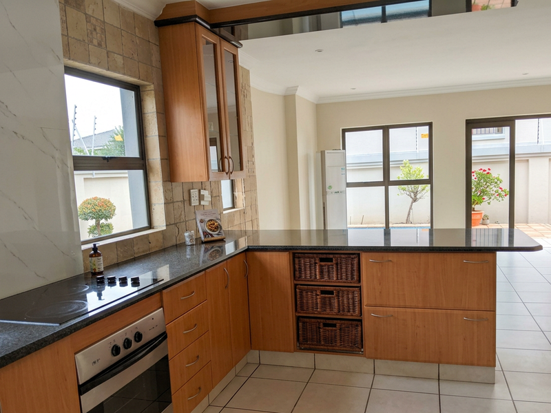 A functional kitchen featuring wooden cabinetry, granite countertops, a built-in oven, and an electric hob, with an open-plan layout and tiled flooring.
