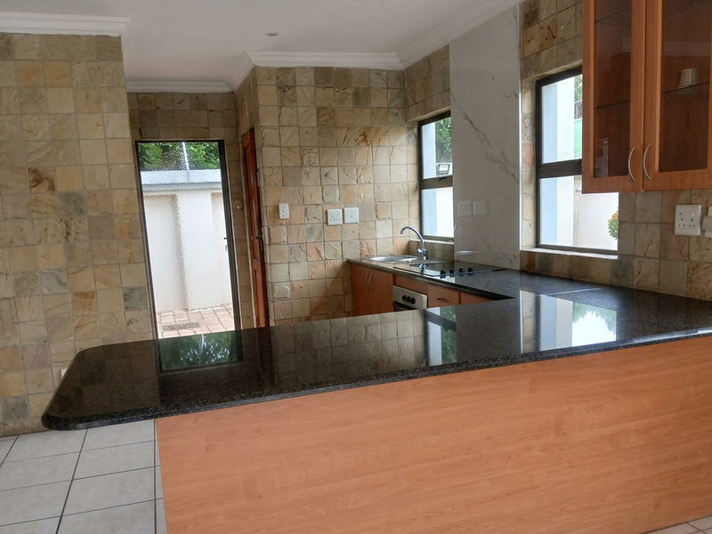 A functional kitchen featuring granite countertops, a breakfast bar, built-in oven, hob, and distinctive stone tile wall cladding with ample natural light.