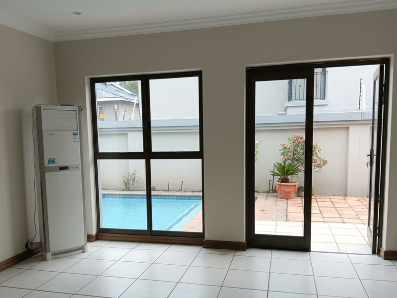 Bright living area featuring tiled flooring and large aluminium doors opening directly onto a private patio and swimming pool area.