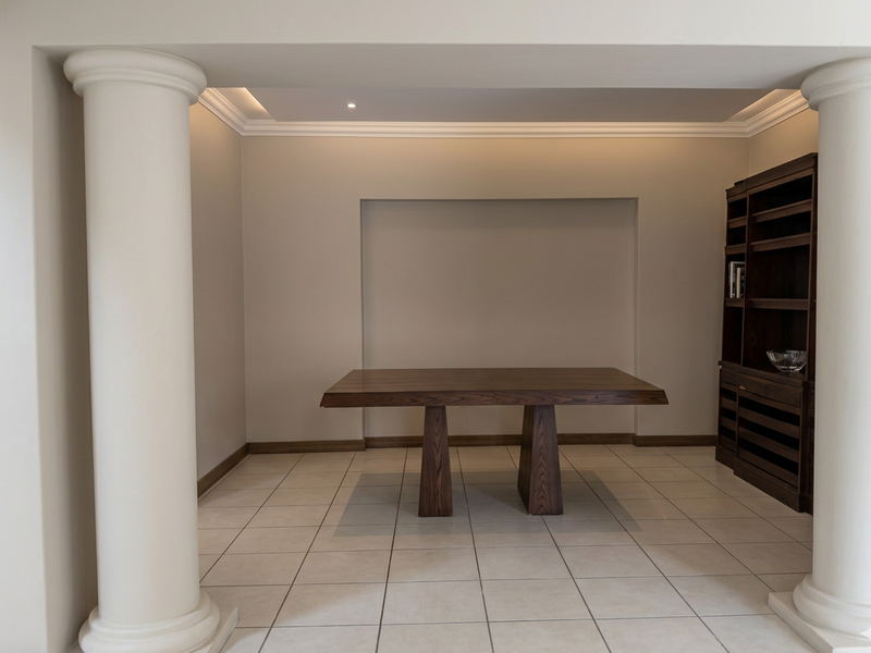 A formal dining area featuring architectural columns, recessed ceiling lighting, crown molding, and neutral ceramic floor tiles.