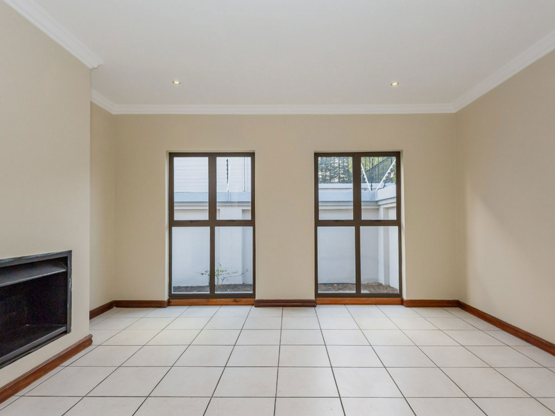 A bright, empty living room featuring neutral walls, tiled flooring, crown molding, and a built-in fireplace with large windows overlooking a private courtyard.