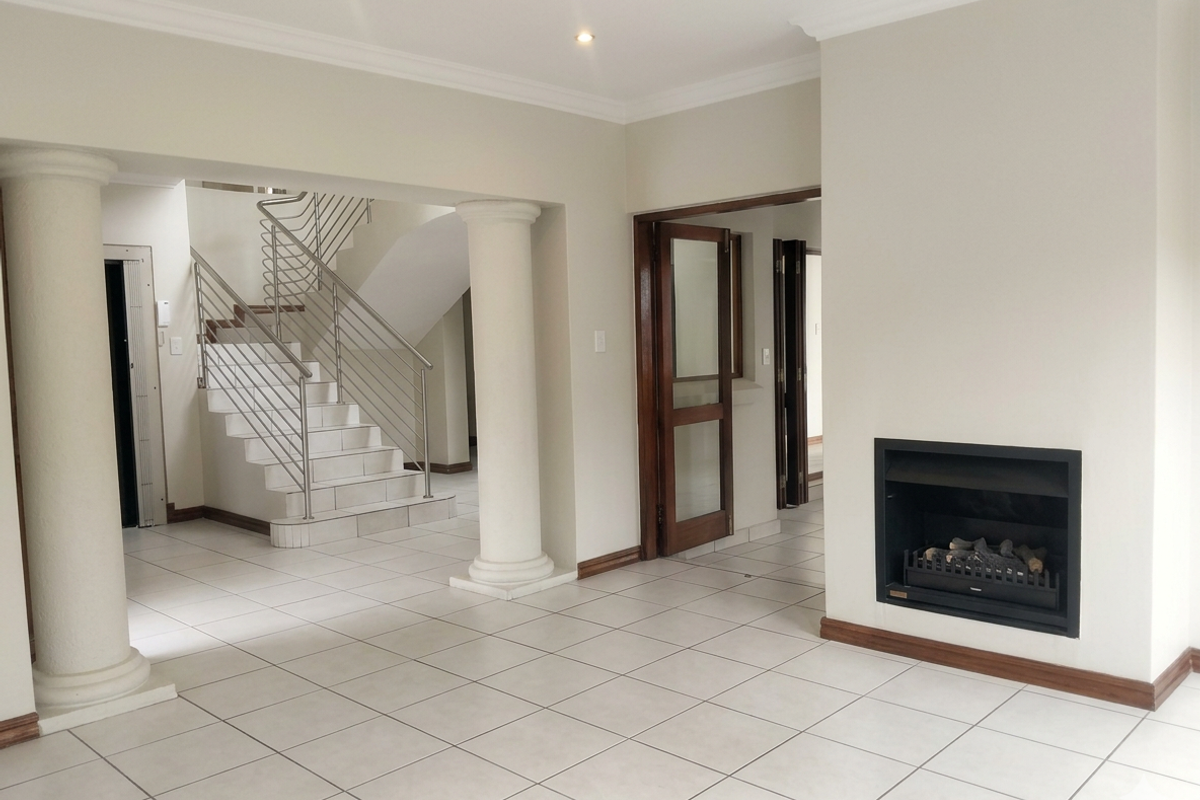 Spacious living area featuring a built-in fireplace, tiled flooring, and an elegant staircase with stainless steel balustrades.