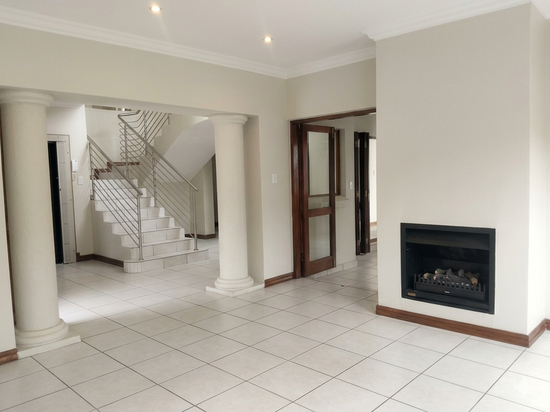 Spacious living area featuring a built-in fireplace, tiled flooring, and an elegant staircase with stainless steel balustrades.