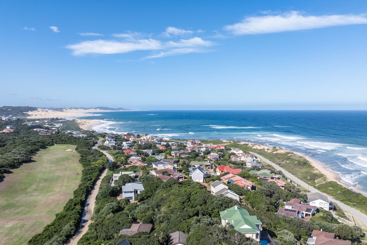 An elevated aerial view of a coastal residential estate situated along the coastline, showcasing the surrounding landscape and proximity to the ocean.