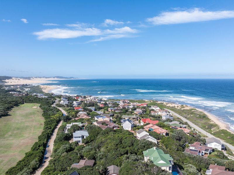 An elevated aerial view of a coastal residential estate situated along the coastline, showcasing the surrounding landscape and proximity to the ocean.