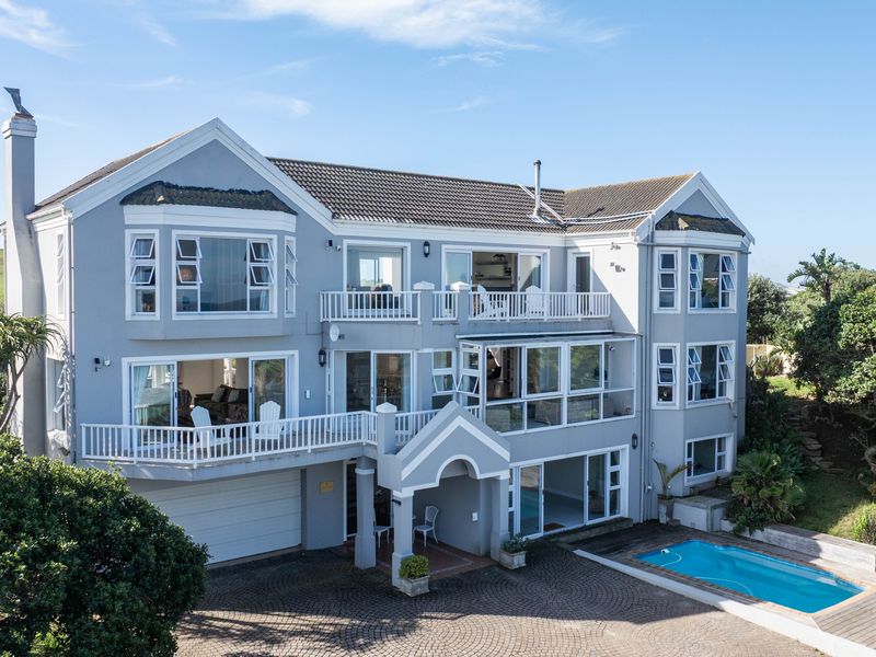 Rear view of a multi-story residential property featuring multiple balconies, a swimming pool, and a paved driveway area.