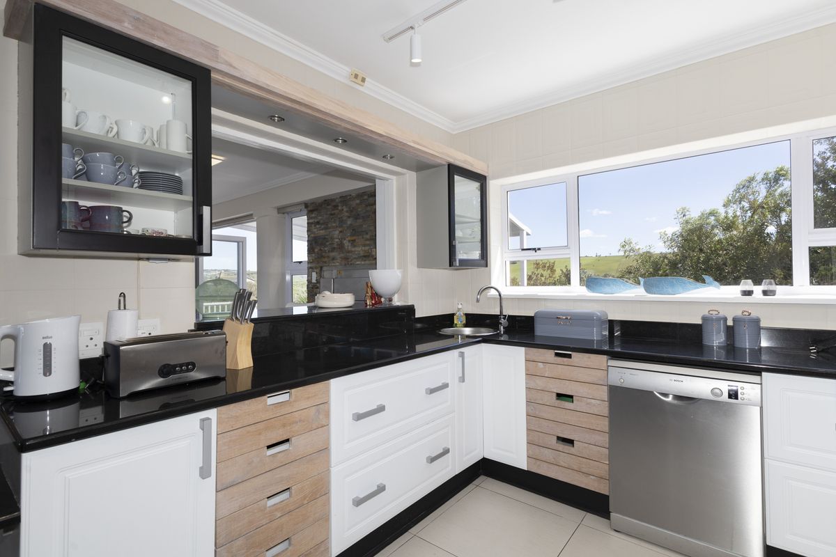 Modern kitchen featuring contrasting white and wood-grain cabinetry, black granite countertops, integrated dishwasher, and large window with natural light.