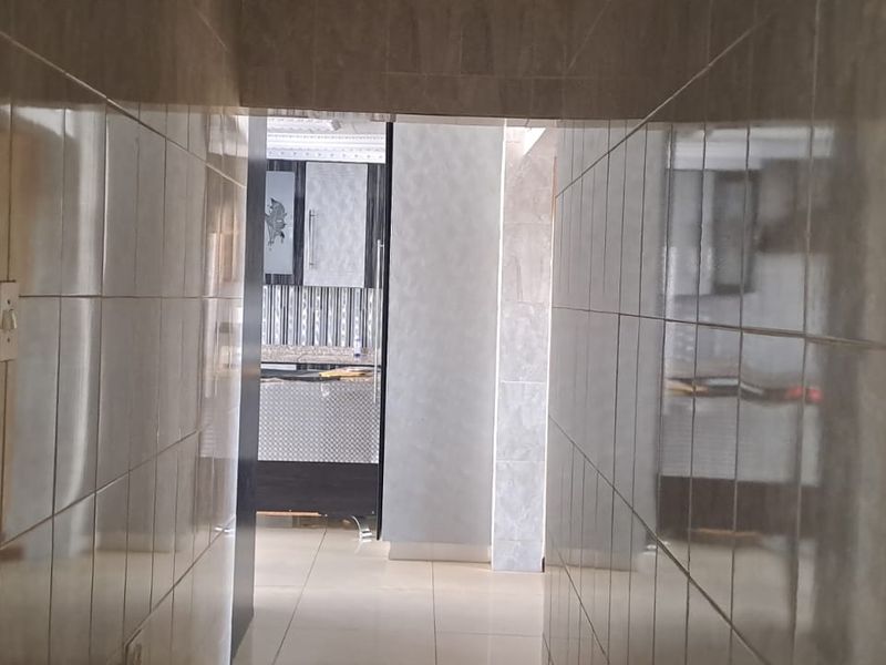 A tiled hallway providing a transition between living spaces, featuring neutral wall tiles and matching floor tiles.