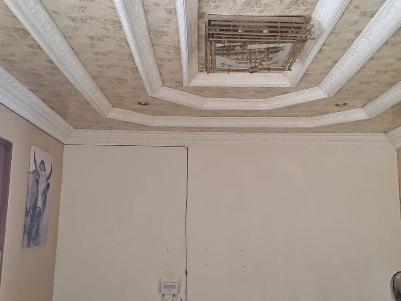 Living room featuring an ornate coffered ceiling with decorative molding and recessed lighting, requiring cosmetic updates to the walls.