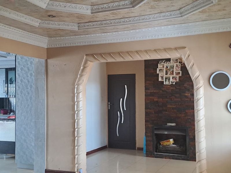 Living room featuring an ornate coffered ceiling, a stone-clad fireplace, and a decorative archway leading to an adjacent space.