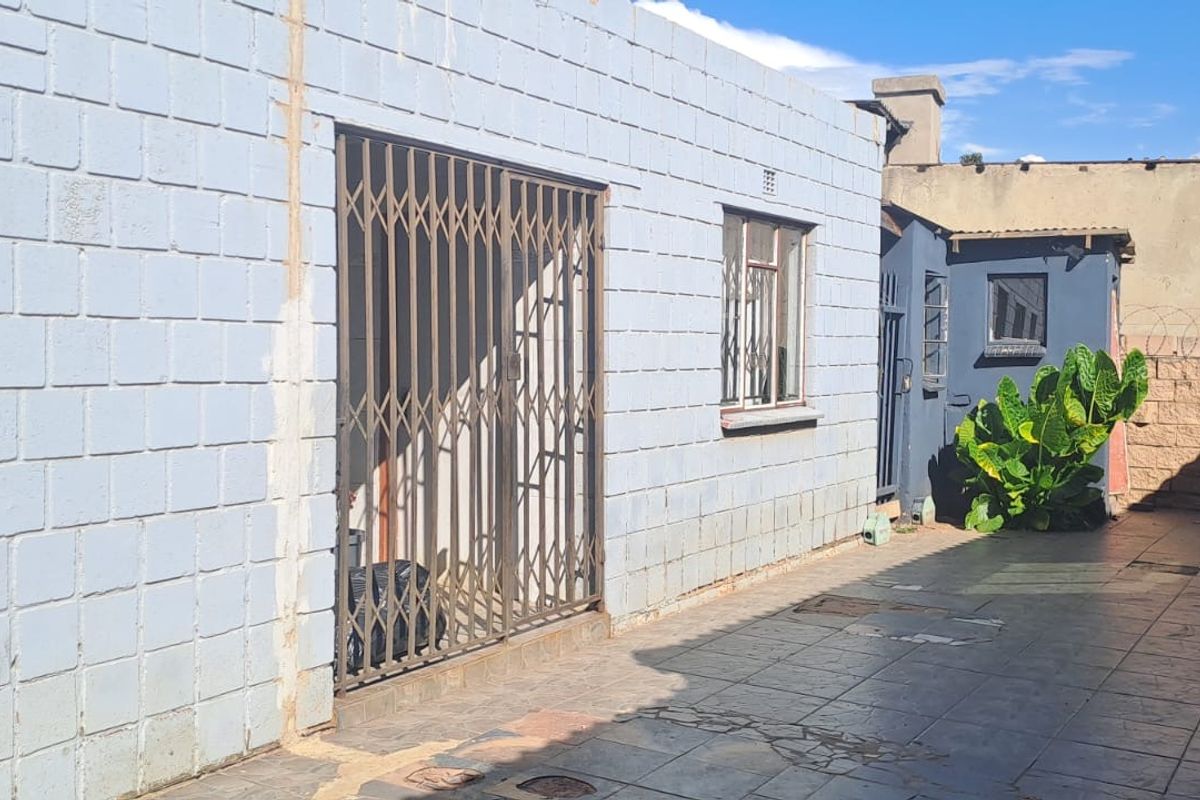 Rear exterior view of the property featuring a tiled patio area, security gates, and concrete block walling with perimeter security.