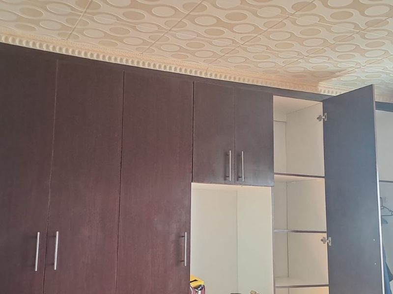 Bedroom featuring dark built-in cupboards and venetian blinds, with visible water damage on the textured ceiling tiles.