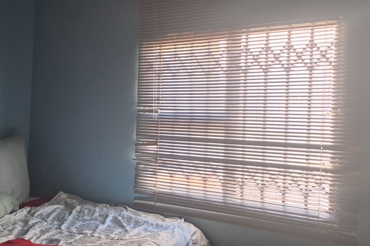 A bedroom featuring a window with security bars and fitted venetian blinds.