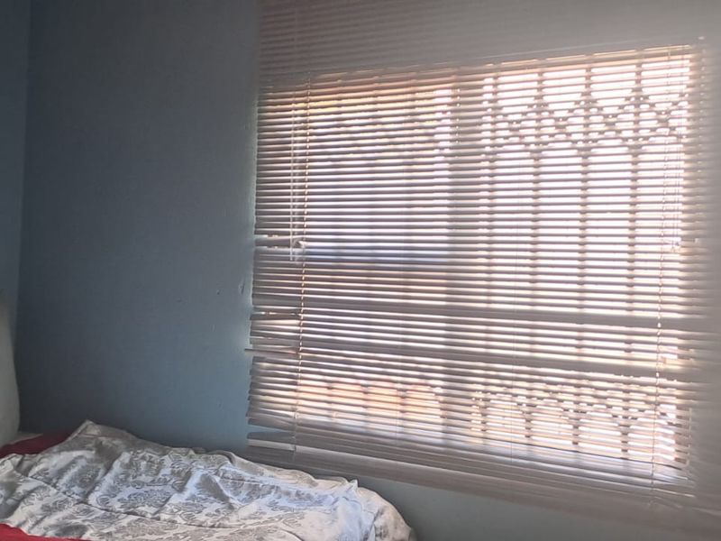 A bedroom featuring a window with security bars and fitted venetian blinds.