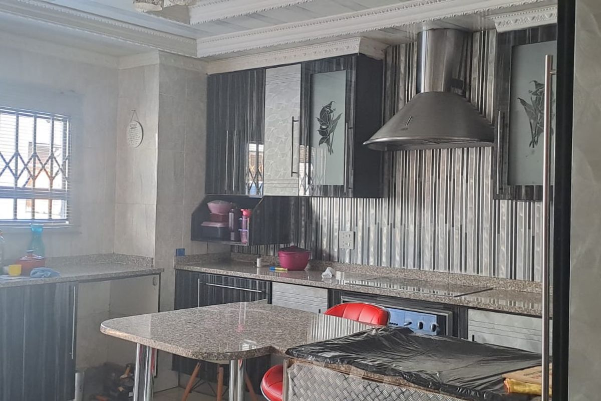 A functional kitchen featuring dark cabinetry, granite countertops, a stainless steel extractor fan, and built-in cooking appliances with security bars on the window.