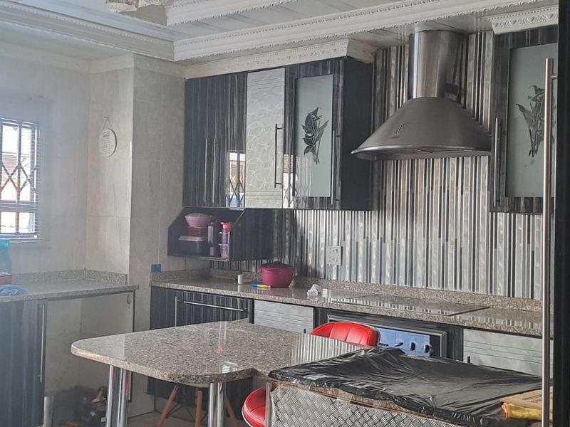 A functional kitchen featuring dark cabinetry, granite countertops, a stainless steel extractor fan, and built-in cooking appliances with security bars on the window.
