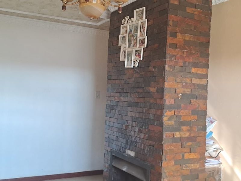 A living room featuring a prominent brick fireplace, decorative ceiling cornices, and a central ceiling rose, offering a classic foundation for renovation.