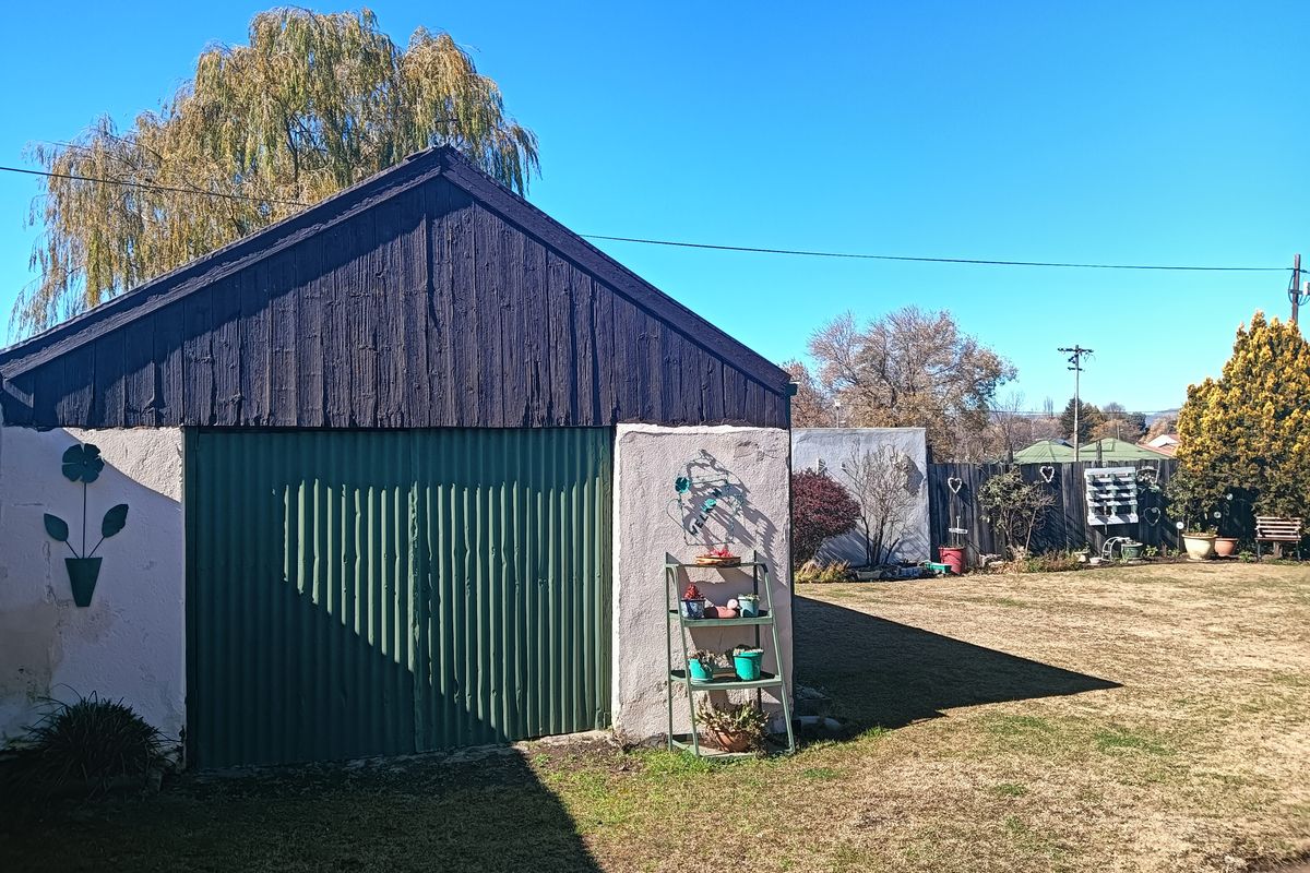 A view of the rear garden featuring a detached garage with corrugated metal doors and timber gable detailing.