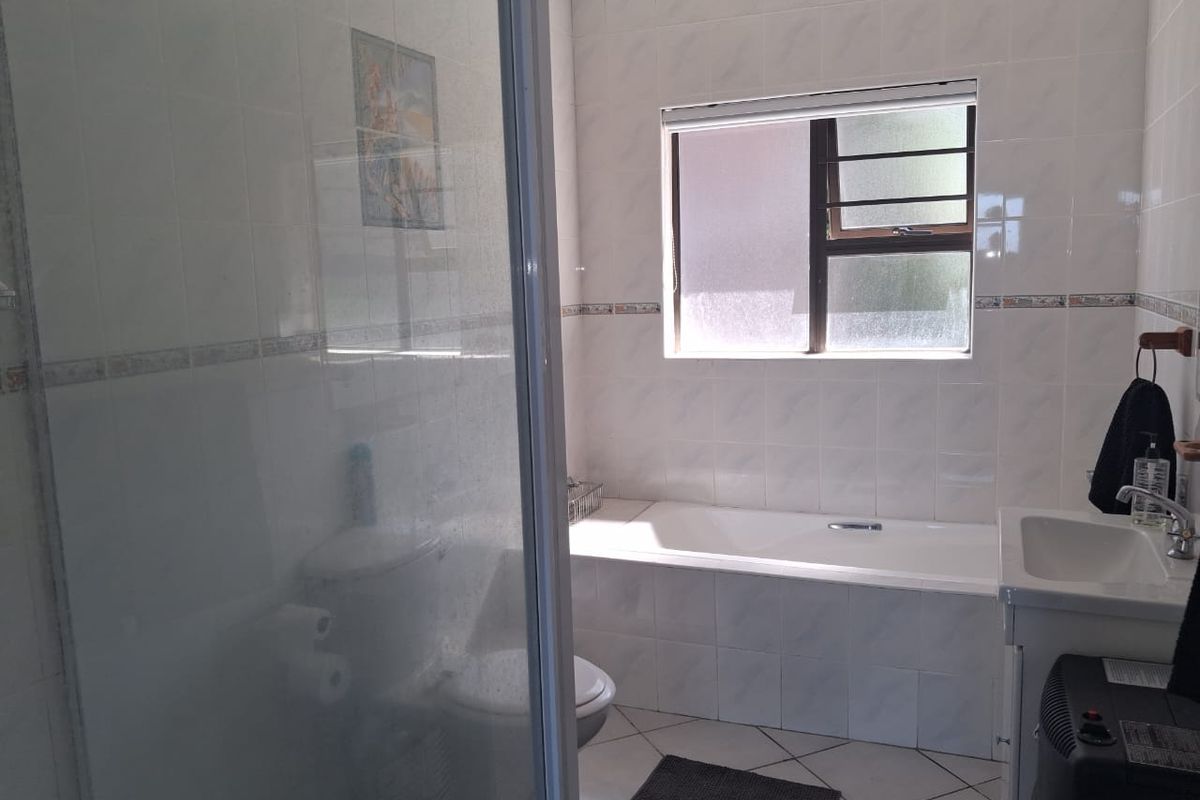 A functional bathroom featuring a built-in bathtub, a separate glass-enclosed shower, and a vanity basin with tiled walls and flooring.