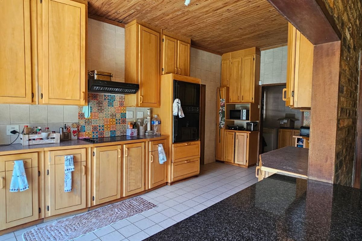 A spacious kitchen featuring extensive wooden cabinetry, granite countertops, a built-in oven, and a decorative tiled backsplash with a warm wooden ceiling.