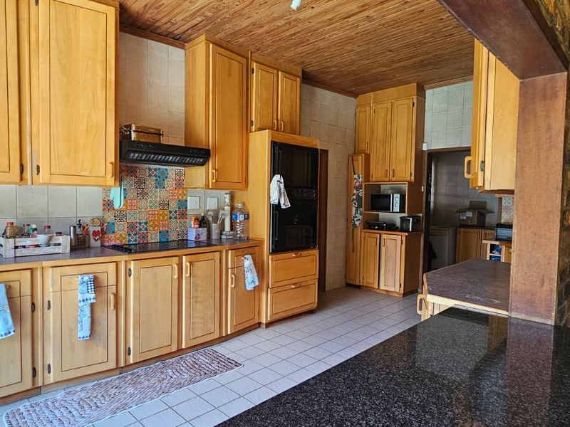 A spacious kitchen featuring extensive wooden cabinetry, granite countertops, a built-in oven, and a decorative tiled backsplash with a warm wooden ceiling.
