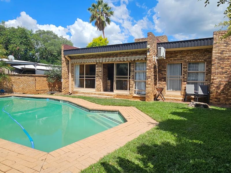 Rear view of the property featuring a brick facade, sliding glass doors with an awning, and a private swimming pool set within a garden.