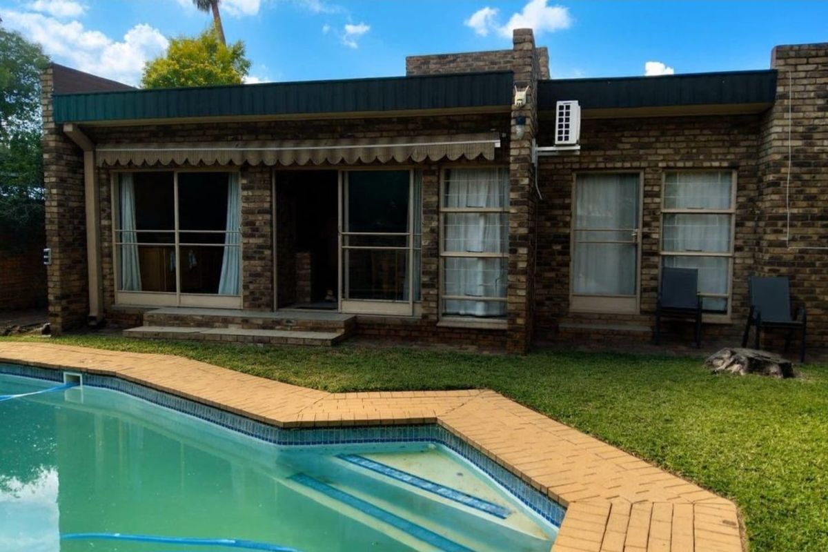 Rear exterior view of the house featuring a brick facade, sliding glass doors with an awning, and a swimming pool with brick coping.