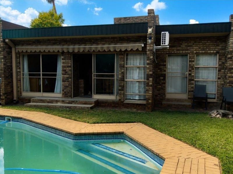 Rear exterior view of the house featuring a brick facade, sliding glass doors with an awning, and a swimming pool with brick coping.