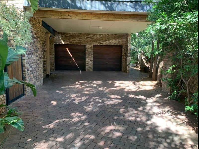 A double garage with timber doors and a covered carport area, featuring brick paving and exposed brick wall finishes.