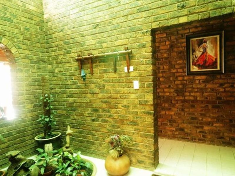 An interior entrance area featuring rustic exposed brick walls, tiled flooring, and an arched window providing natural light.