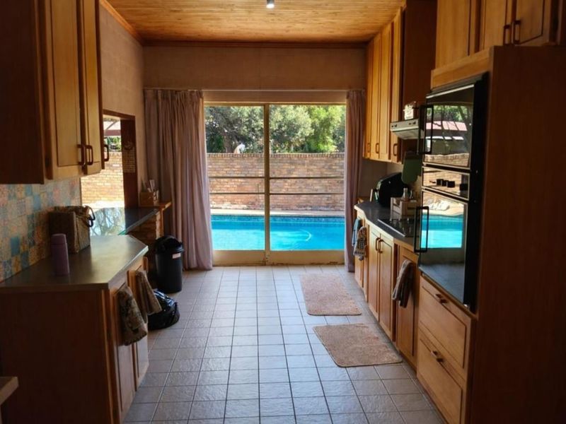 A functional kitchen featuring wooden cabinetry, built-in appliances, and tiled flooring, with direct access to the outdoor pool area through a sliding glass door.