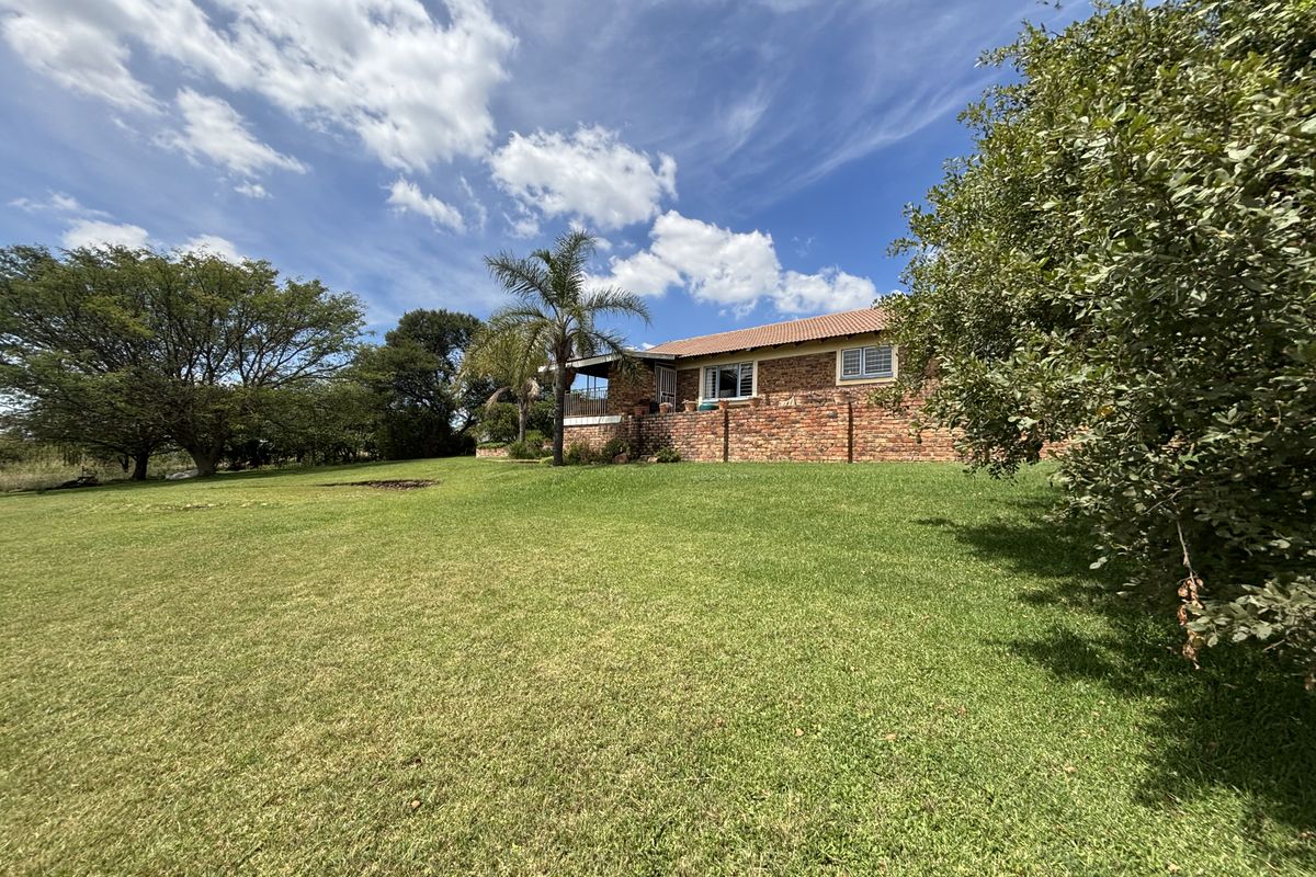 A view of the rear elevation of the face-brick home, featuring a covered patio area and expansive surrounding lawn.
