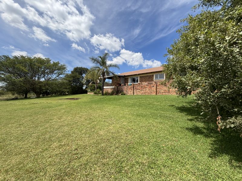 A view of the rear elevation of the face-brick home, featuring a covered patio area and expansive surrounding lawn.