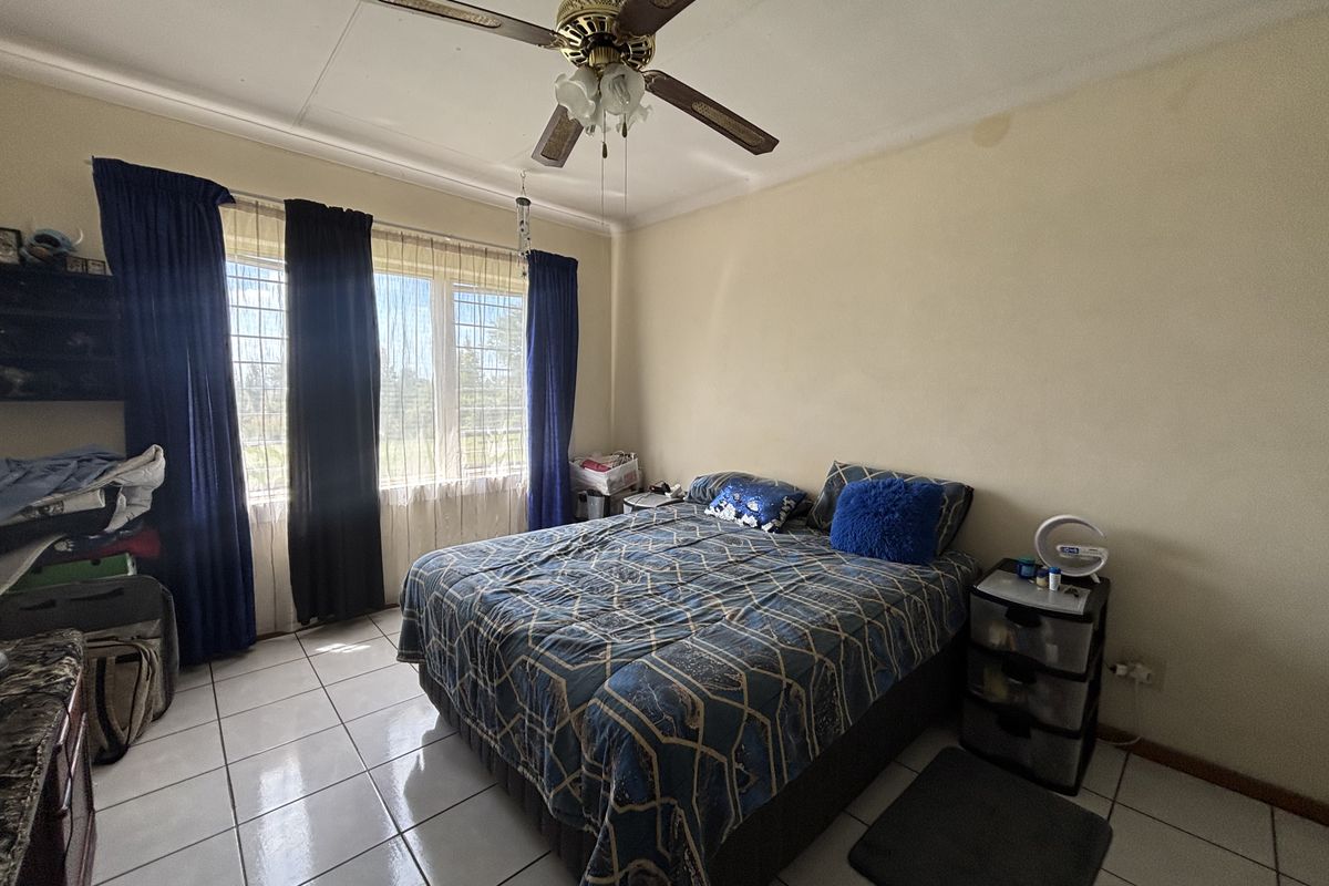 A bedroom featuring tiled flooring, a ceiling fan, and security bars on the windows, with visible water staining on the ceiling.