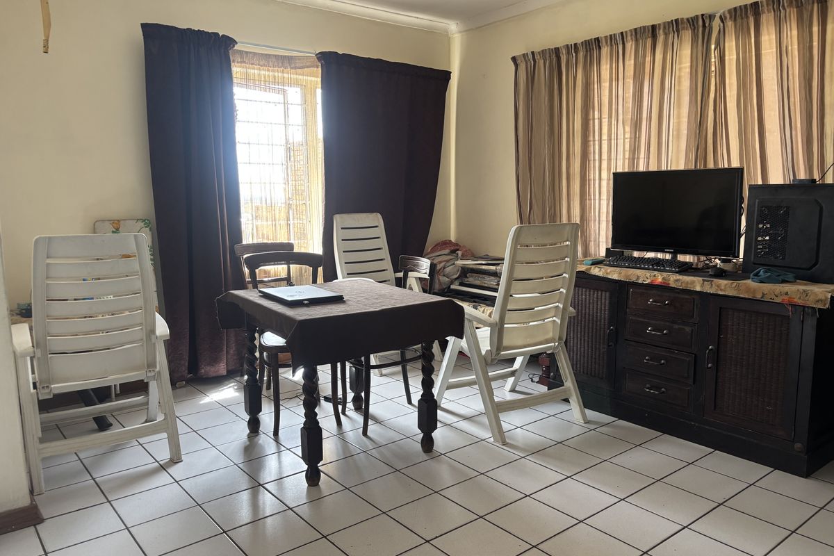 A living area featuring tiled flooring and large windows with curtain rails, providing a functional space that could benefit from cosmetic updates.