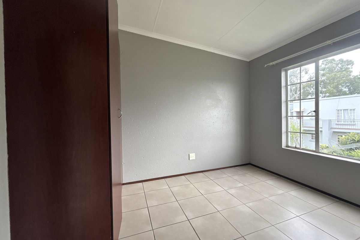 A vacant bedroom featuring neutral tiled flooring, a built-in cupboard, and a window with security bars, offering a blank canvas for personalization.