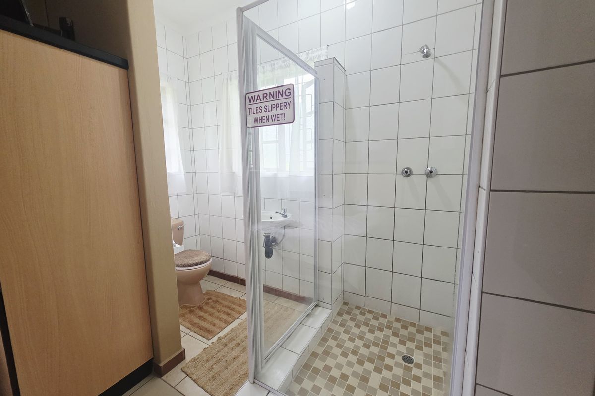 A functional bathroom featuring a glass-enclosed shower, wall-mounted basin, and toilet with white wall tiling and neutral floor tiles.