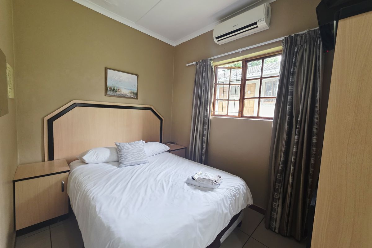 A compact bedroom featuring tiled flooring, a built-in headboard, and a wall-mounted air conditioning unit.