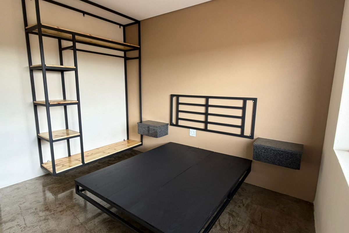 A modern bedroom featuring a polished concrete floor, custom built-in metal shelving, and a wall-mounted headboard with integrated floating bedside tables.