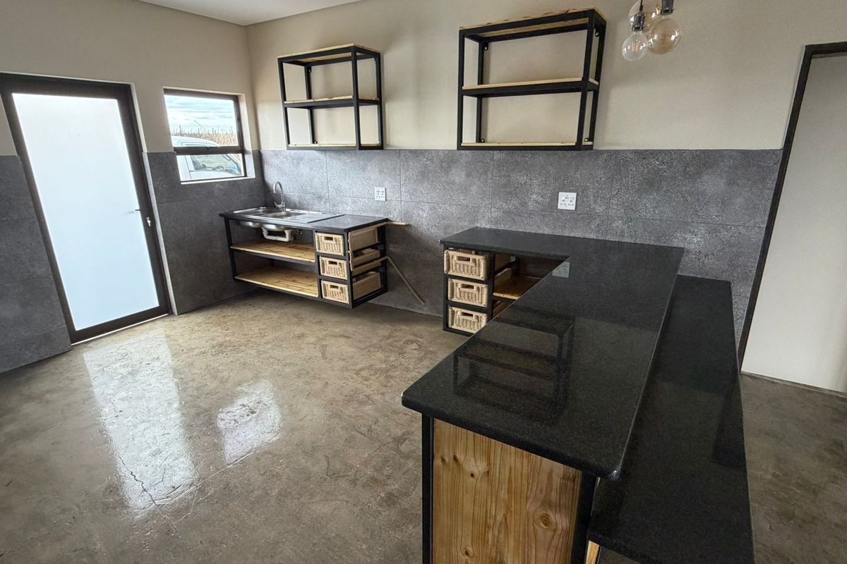 Modern kitchen featuring polished concrete floors, stone countertops, industrial-style open shelving, and a tiled splashback in a clean, minimalist space.