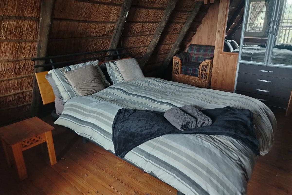A cozy bedroom featuring a unique thatched roof with exposed timber rafters and warm timber flooring, including a built-in wardrobe.