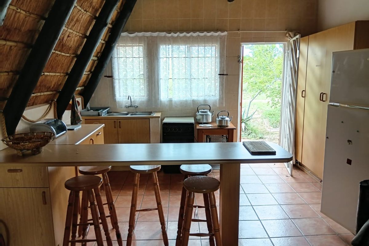 A rustic kitchen featuring a unique thatched roof, exposed timber beams, tiled flooring, and built-in cabinetry with a breakfast bar area.